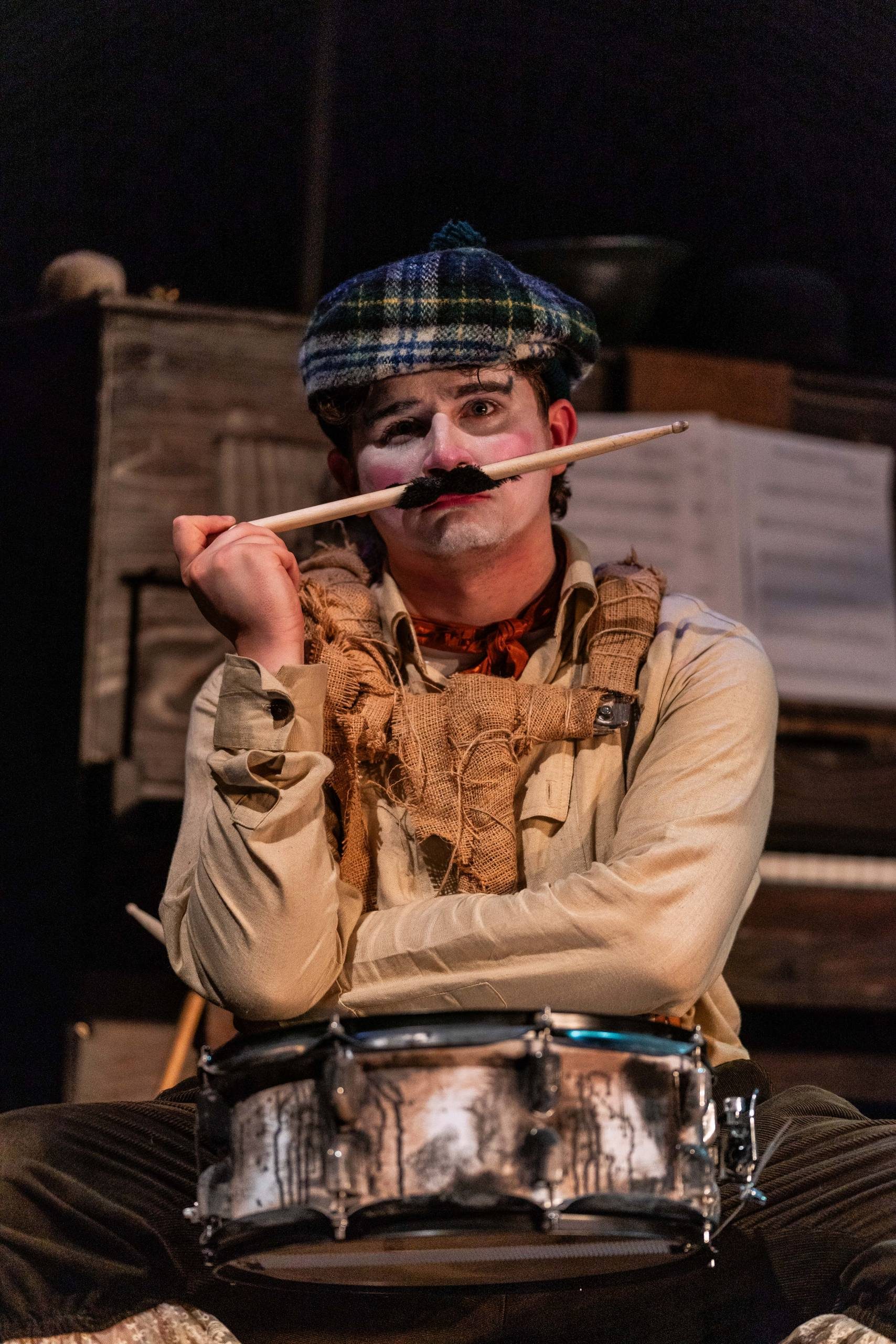 Oh What A Lovely War A man with a drum holds a drumstick with a moustache attached to it to his face.