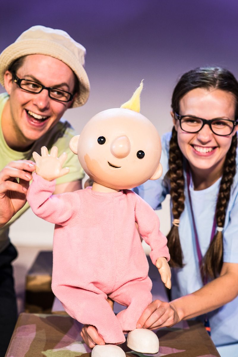 We're Going On A Bear Hunt A baby puppet is waving, the puppet is operated by a male and female character.