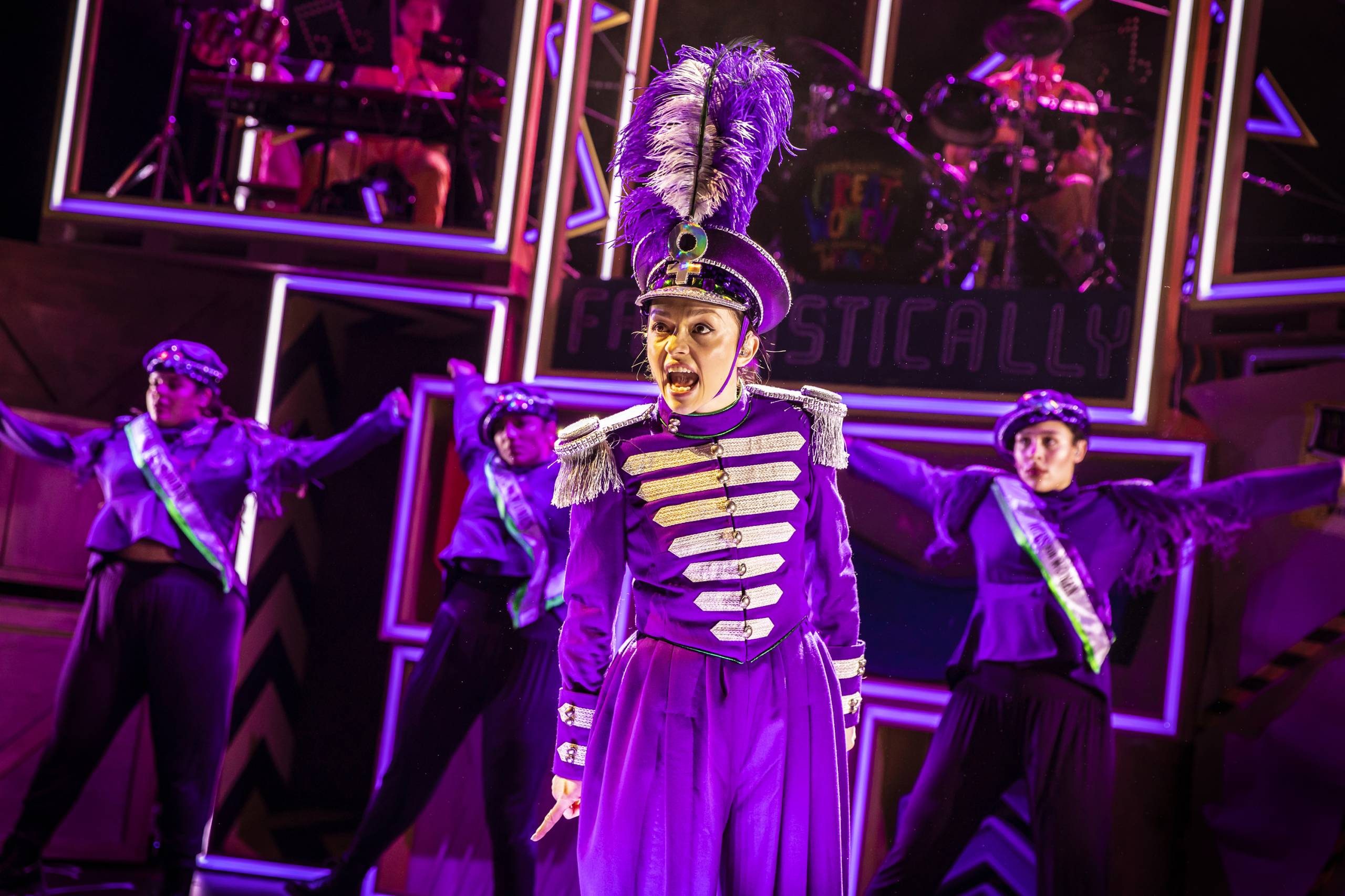 Fantastically Great Women Who Changed The World Four characters are dressed in purple singing and dancing with the band behind them.