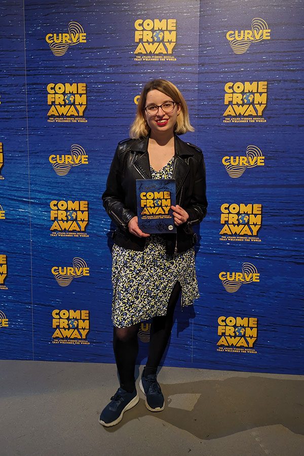 Lydia Greatrix Lydia Greatrix stands in front of a Come From Away publicity board