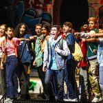 SYP The Lightning Thief The Lightning Thief: The Percy Jackson Musical. The male lead stands centre stage singing while the ensemble of 16 visible young participants sing and point at the male lead.