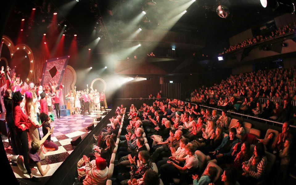 Studio 1 An image of MAST's studio one with a full audience. A colourful and bright performance of Alice in Wonderland is on stage.