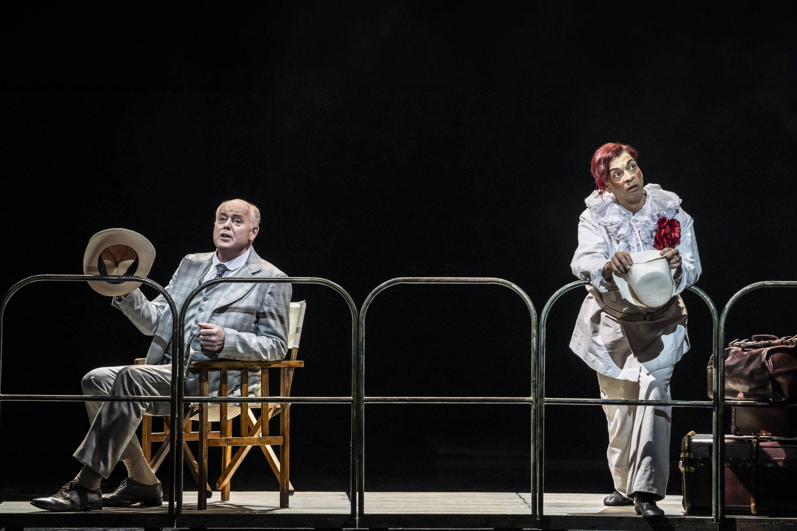 Death in Venice Aschenbach and The Old Man Aschenbach (Mark le Brocq) sits in a chair to the left, The Old Man with dyed red hair leans on the ships railings to the right.